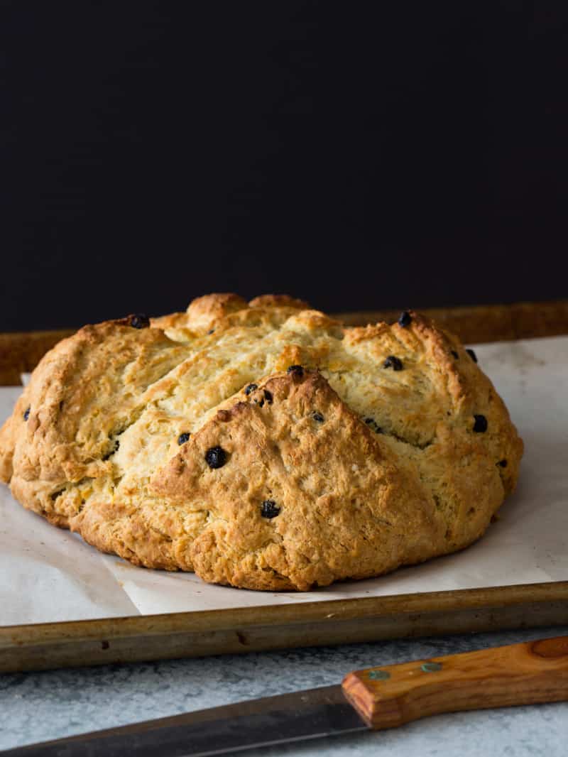 A loaf of Irish soda bread with dried blueberries on a sheet pan with parchment paper.