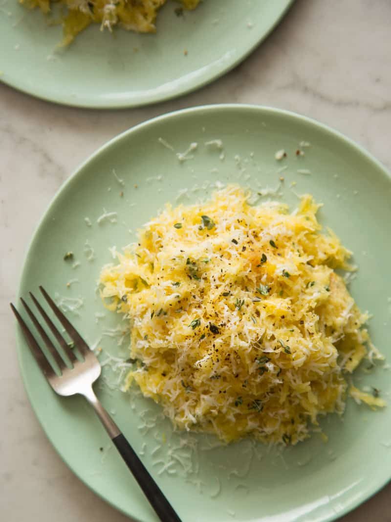 Plates of spaghetti quash with goat cheese and garlic sauce and a fork.