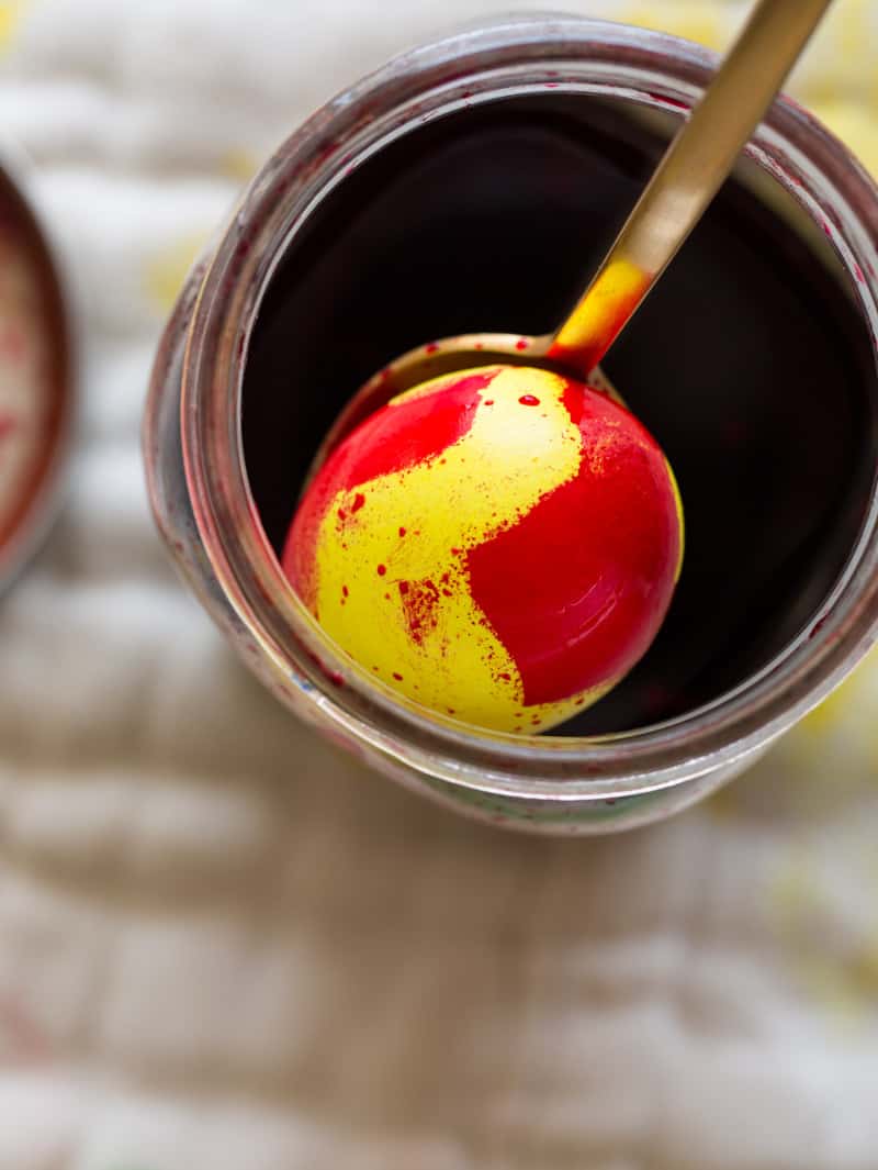 A close up a yellow egg, dipped in red dye and holding the red in some places.