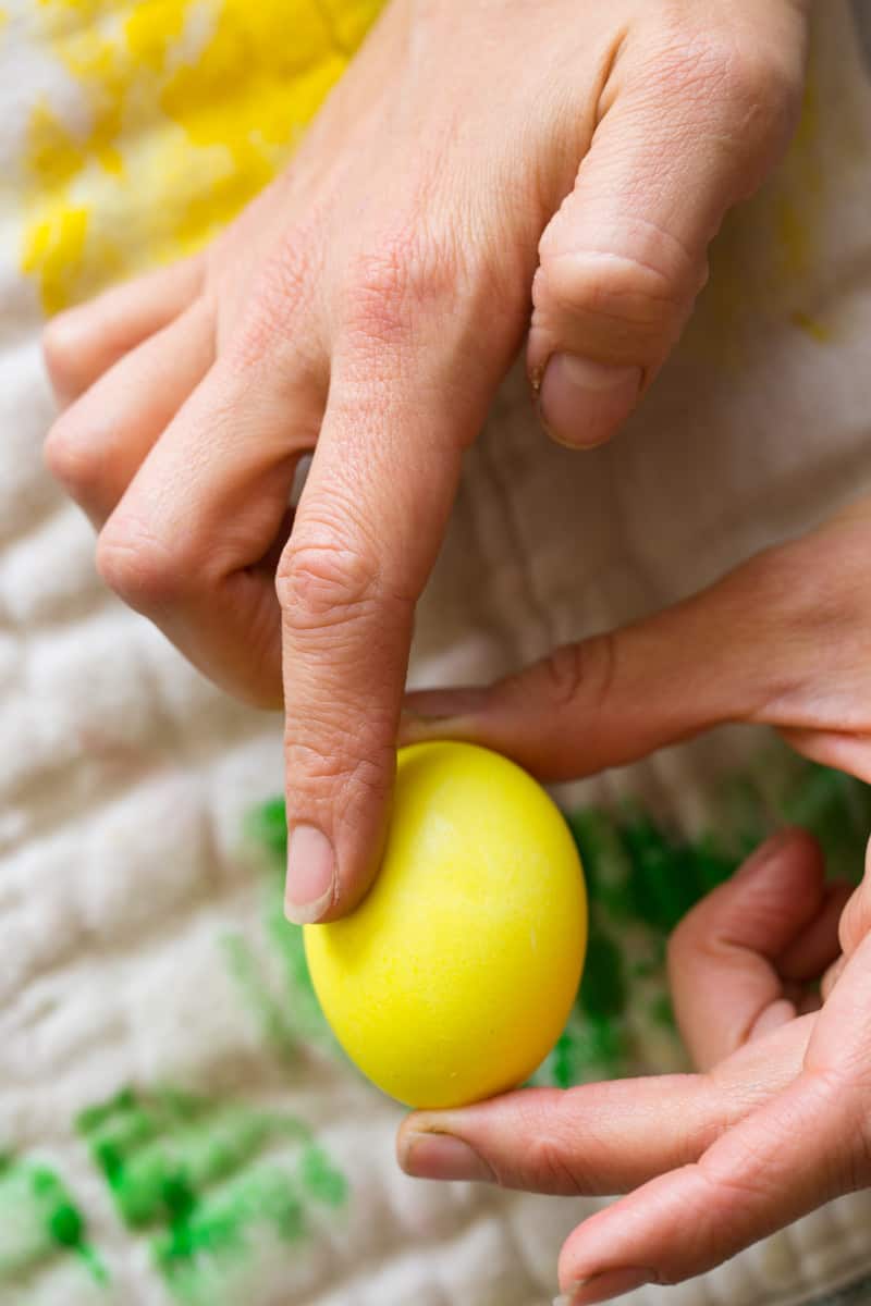 Both hands holding a yellow dyed egg.