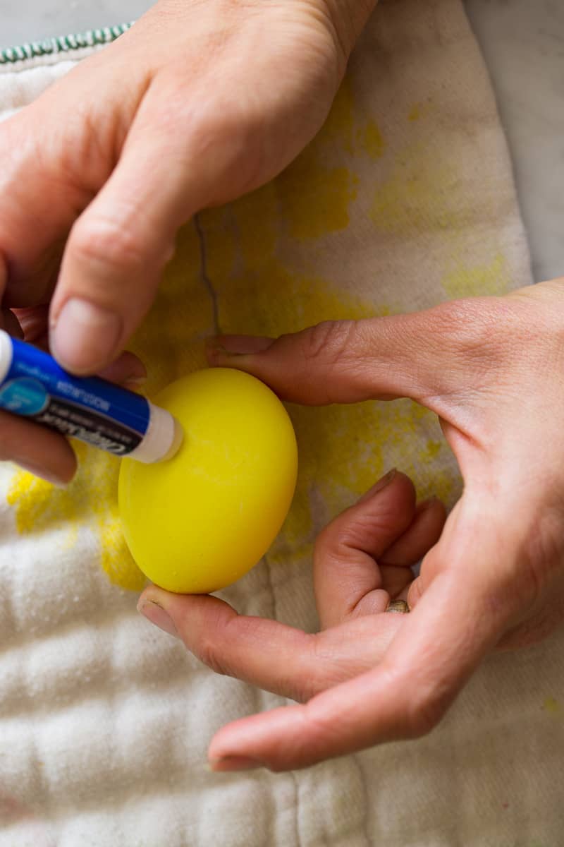 A person holding a yellow egg while putting lip balm on the surface.