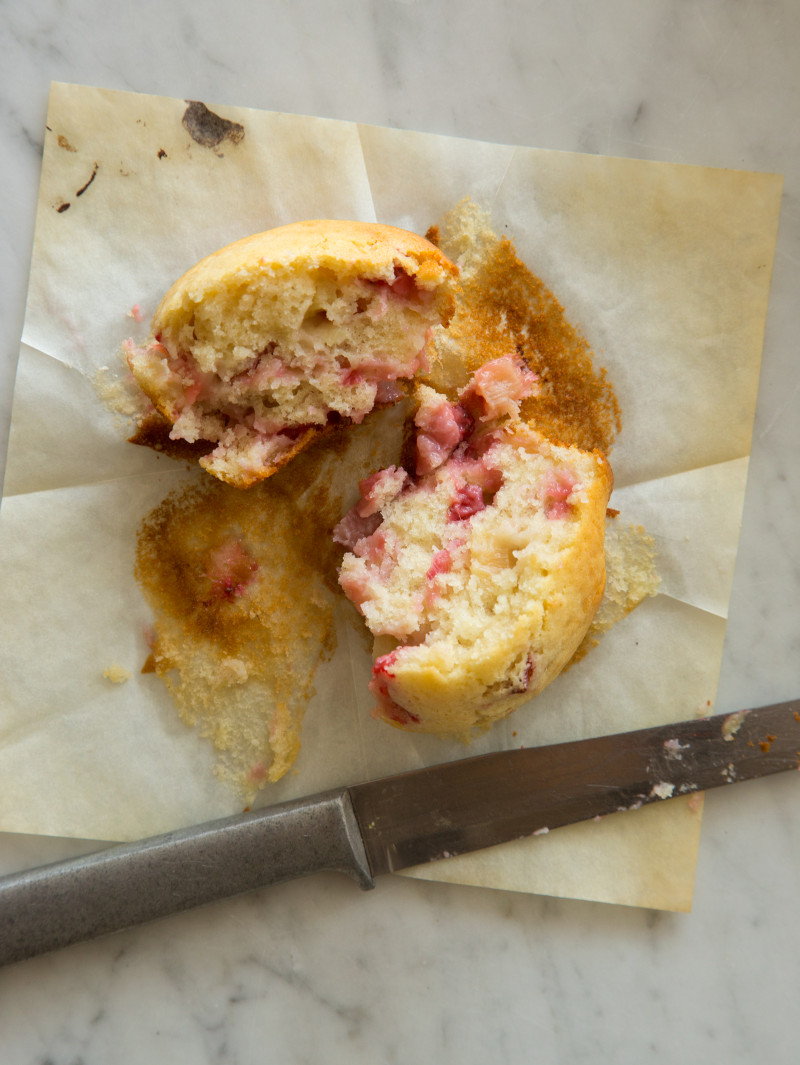 A half eaten brown sugar, strawberry rhubarb muffin with a knife.