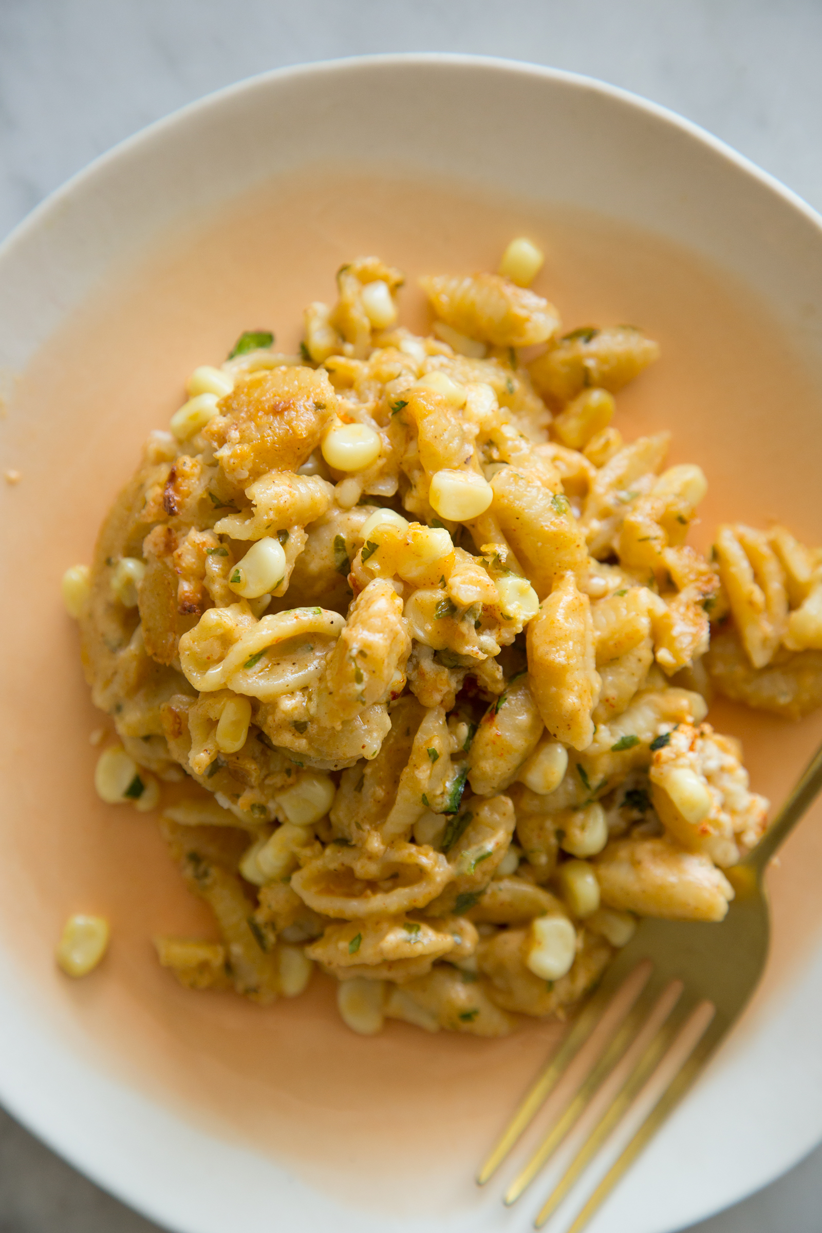 Elote mac and cheese on a plate with a fork next to it.