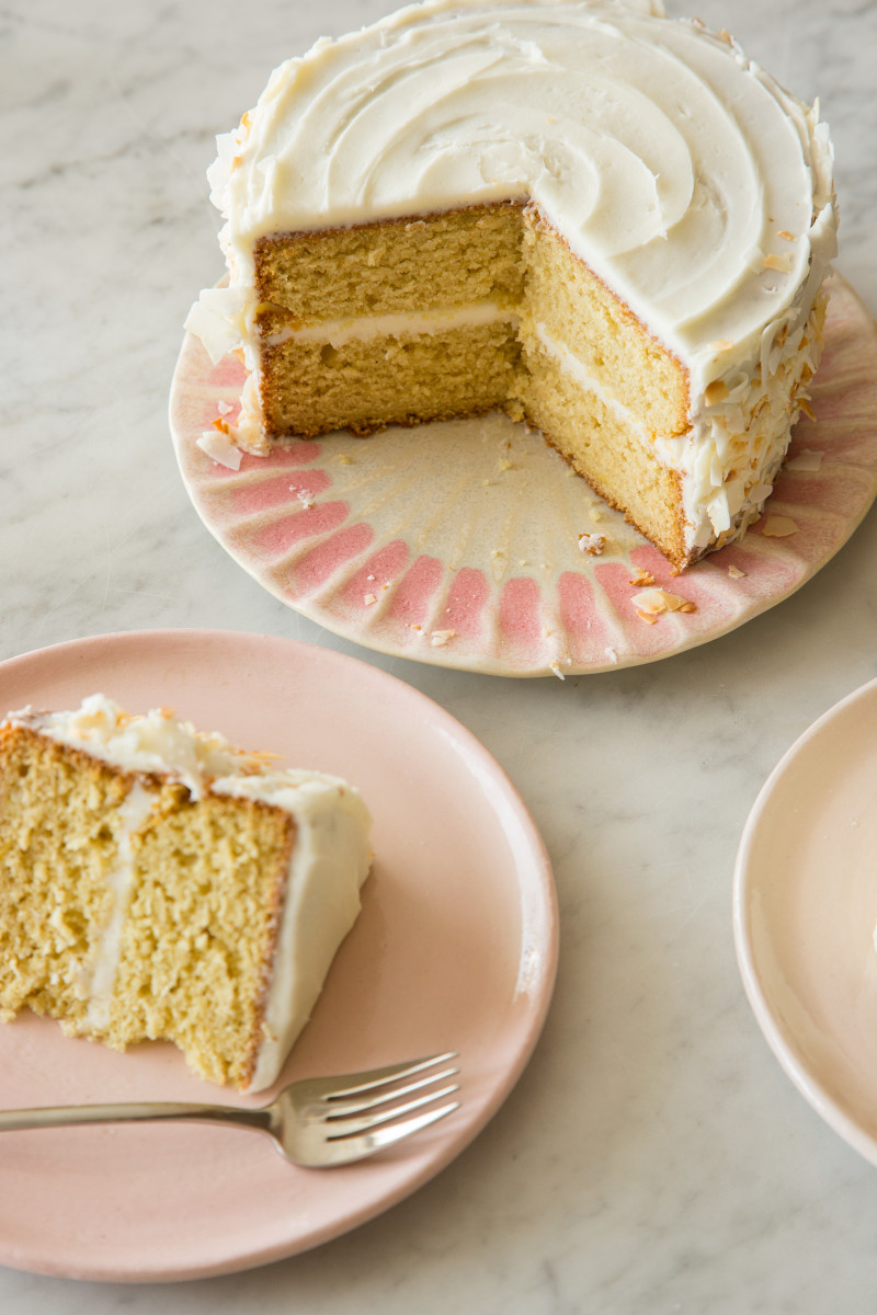 A sliced coconut cake next to a plate with a piece of cake and a fork.