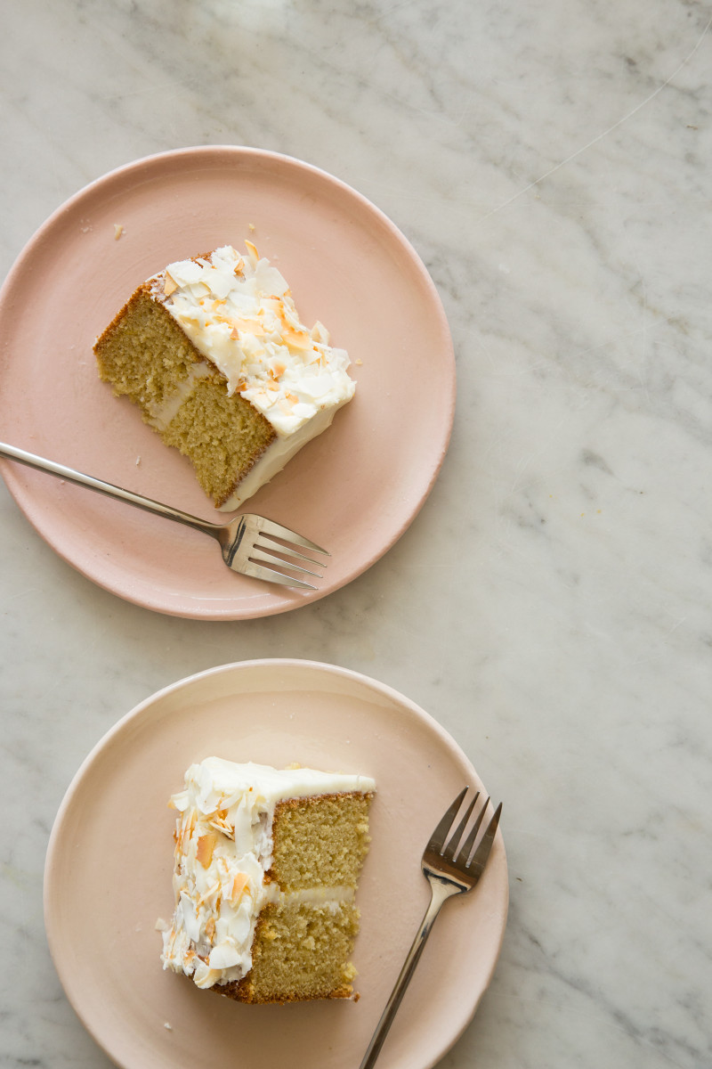 Slices of coconut cake on light pink plates with forks.