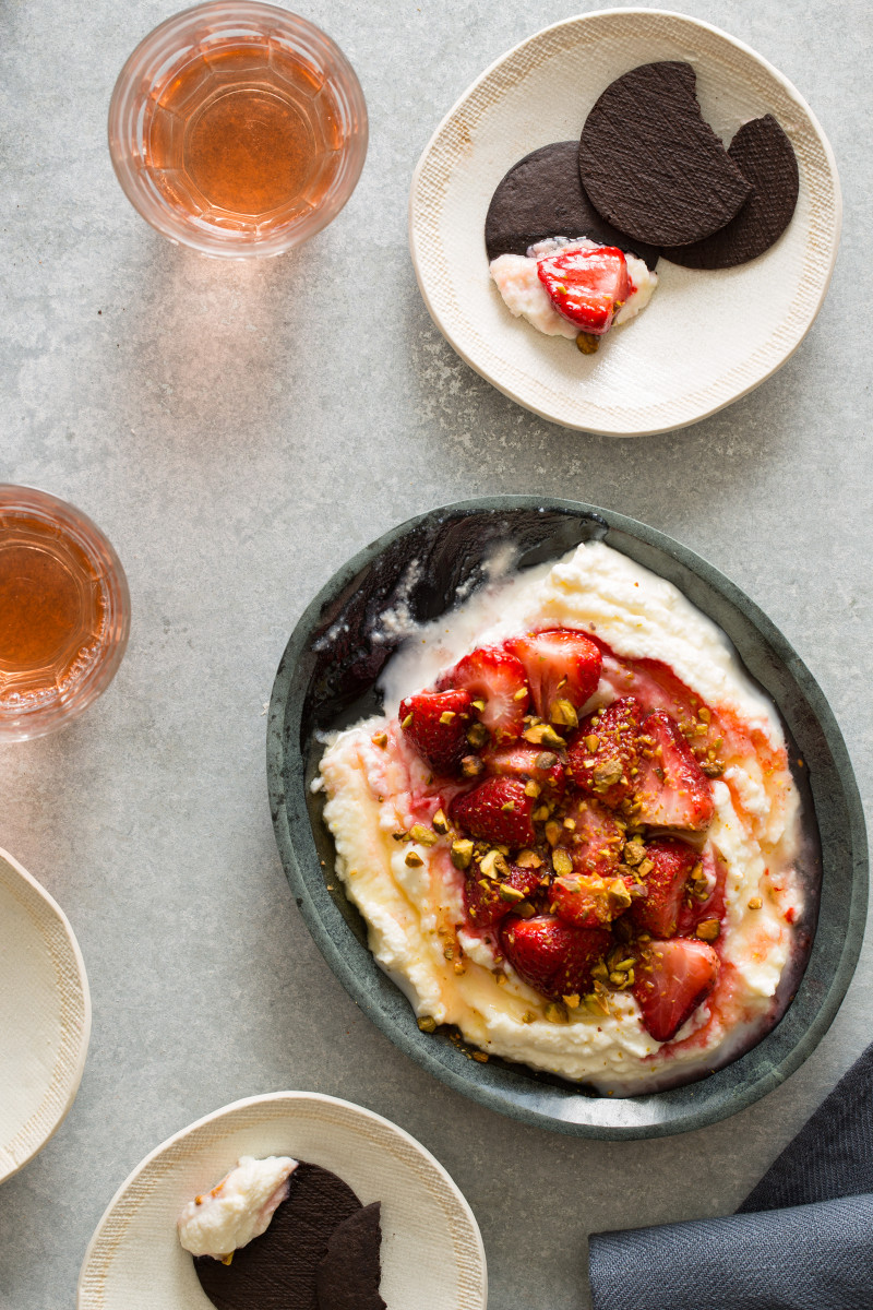 A bowl of roasted strawberries over honey whipped ricotta with a serving on a plate.