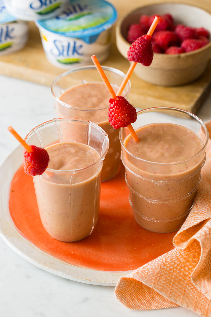 A close up of peach, papaya, and raspberry smoothies garnished with skewered raspberries.