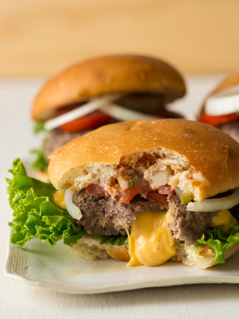 A close up of a juicy lucy burger with a bite taken out and cheese oozing out.