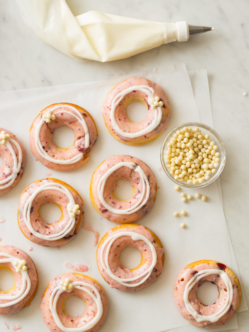 Baked cherry doughnuts with cherry and vanilla glaze with a bowl of white chocolate crispy balls.