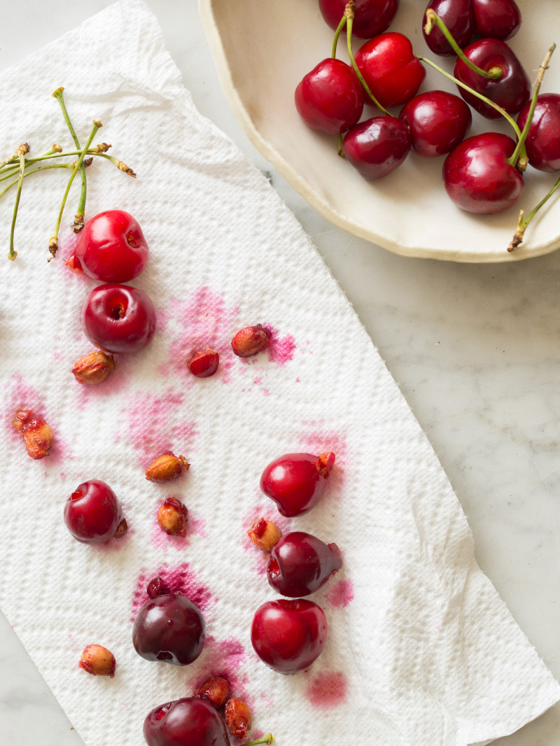 A bowl of fresh cherries next to pitted cherries on a paper towel.