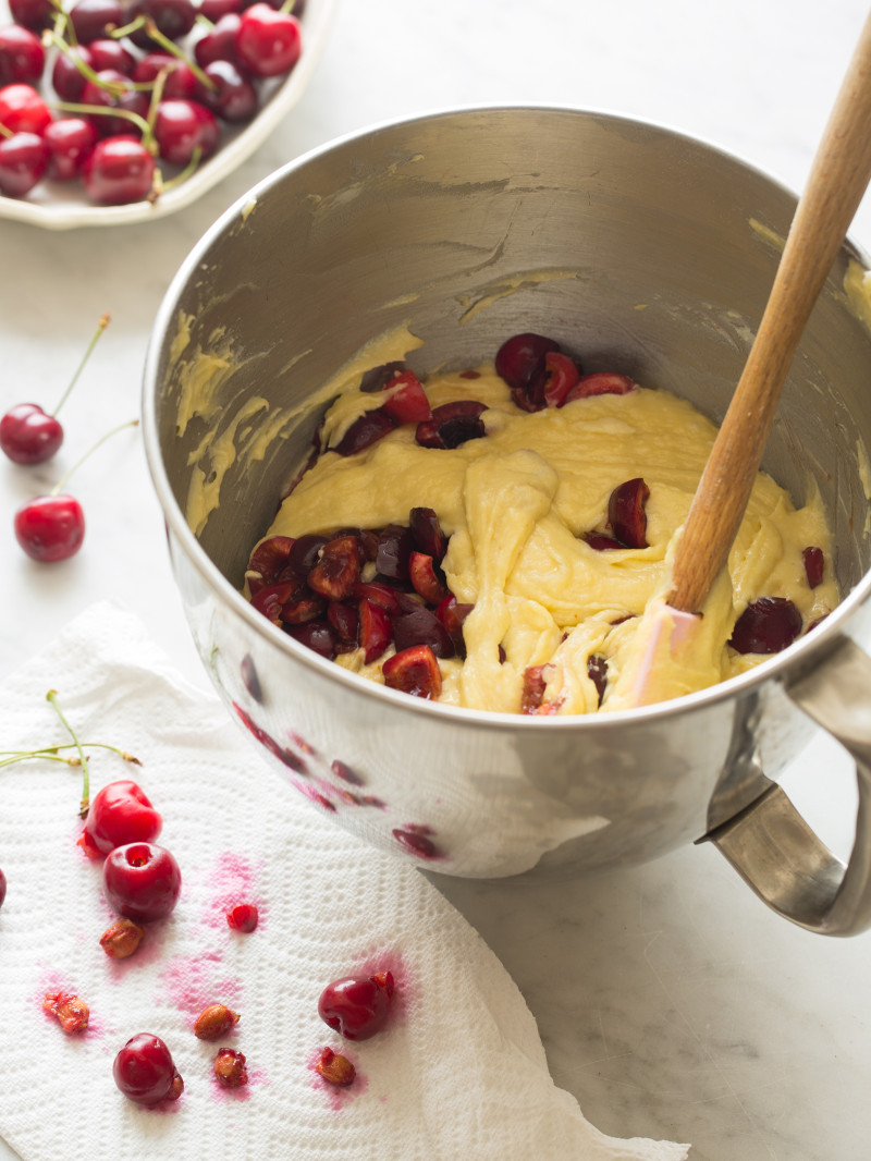 A mixing bowl of batter and cherries being folded in with a spatula.