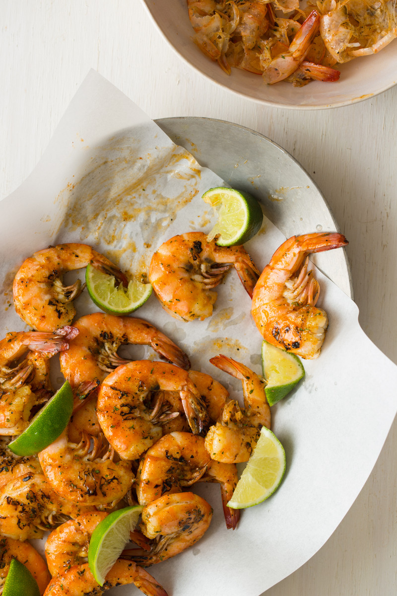 A plate of grilled peel and eat shrimp with lime wedges.