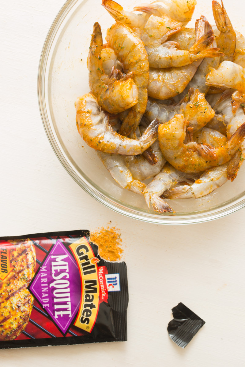 A bowl of raw, seasoned, peel and eat shrimp with a packet of marinade.