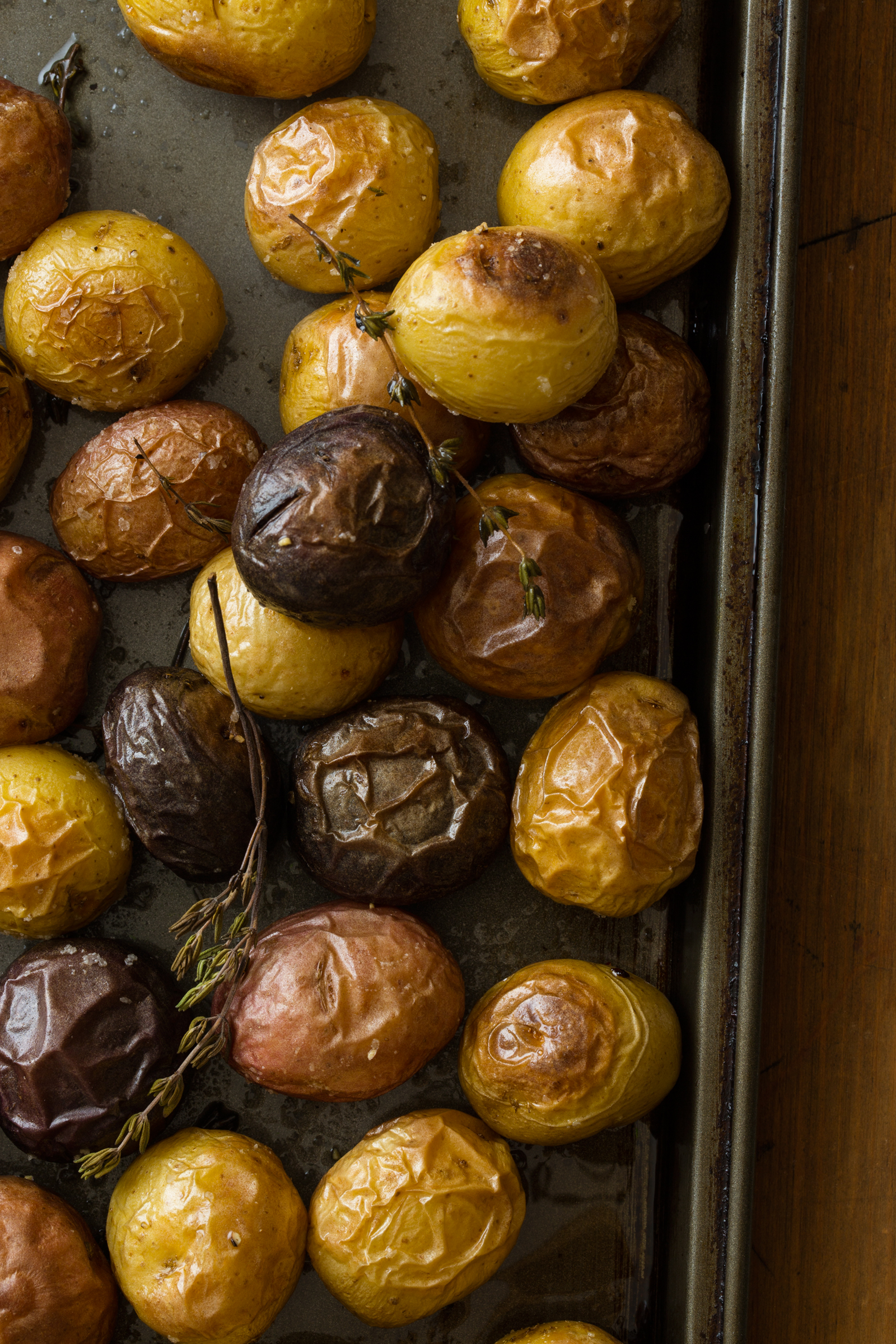 A sheet pan full of roasted potatoes with sprigs of thyme. 