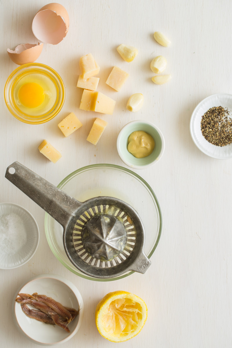 Classic caesar salad dressing ingredients in bowls and a citrus juicer.