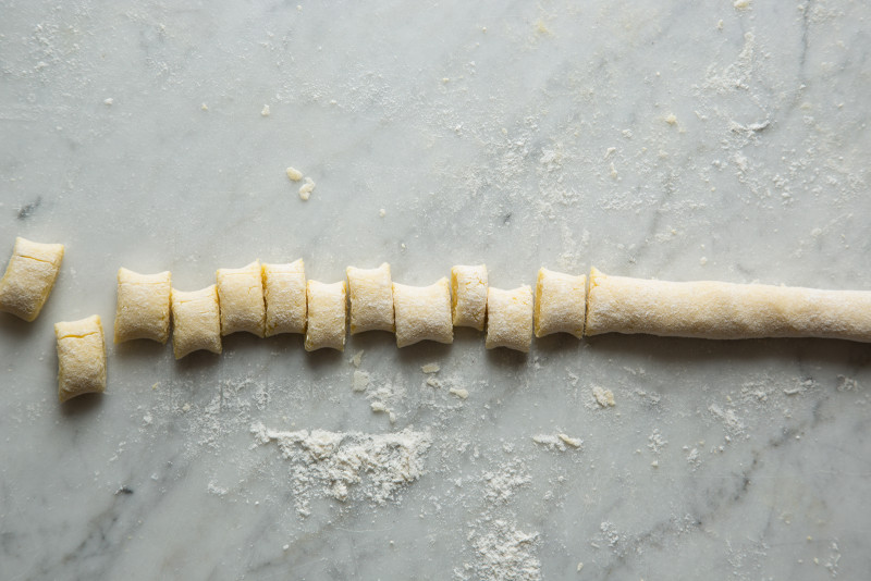 A long piece of dough being cut into gnocchi on a marble surface.