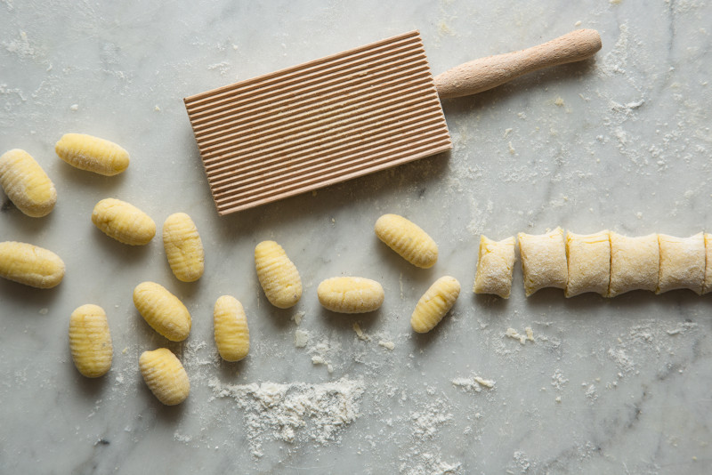 Gnocchi being finished with a gnocchi paddle on a marble surface.