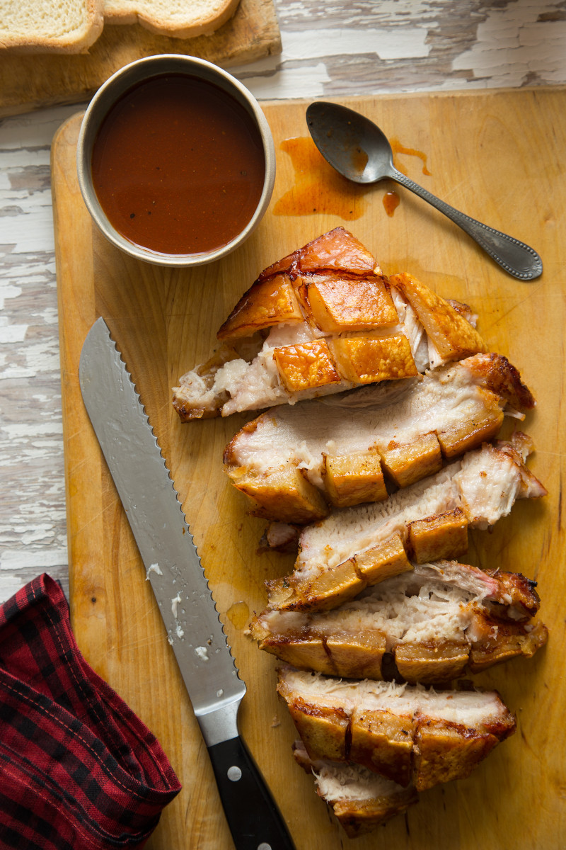 Sliced crispy grilled pork belly with sweet and tangy vinegar BBQ sauce on the side.