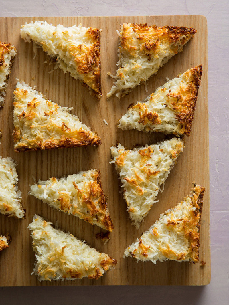 Several triangle cut pieces of coconut oat bars on a wooden cutting board.