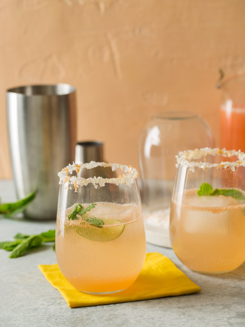 Several glasses of paloma with mint leaves and a cocktail shaker.