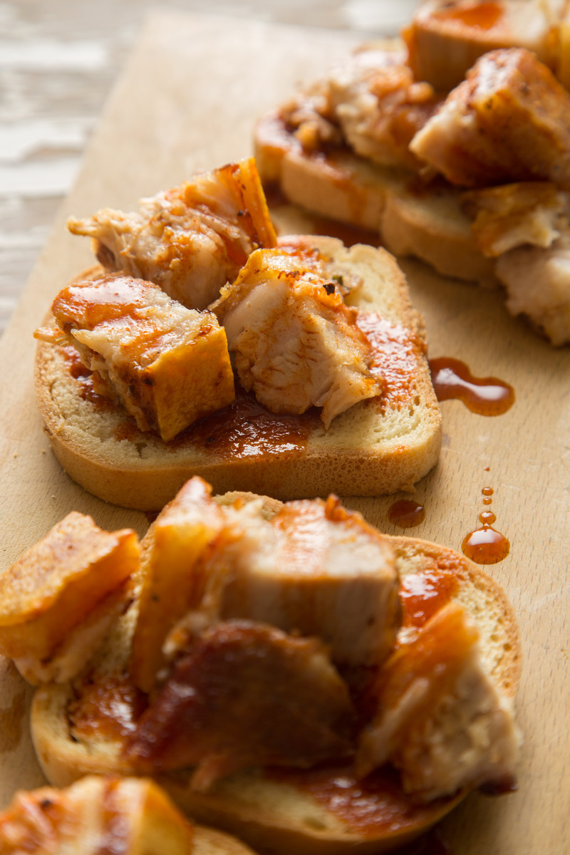 A close up of grilled pork belly with sweet and tangy vinegar BBQ sauce on bread.