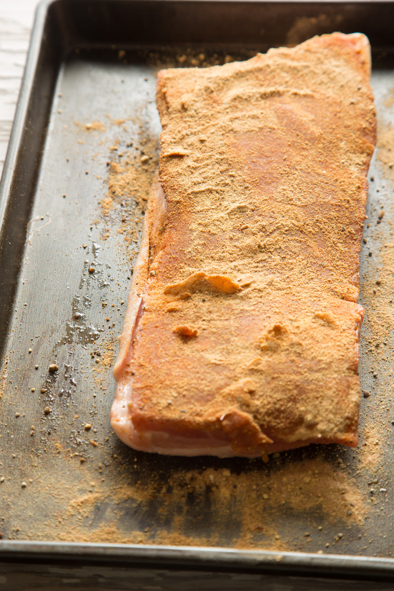 A close up of raw pork belly with dry rub on a sheet pan.