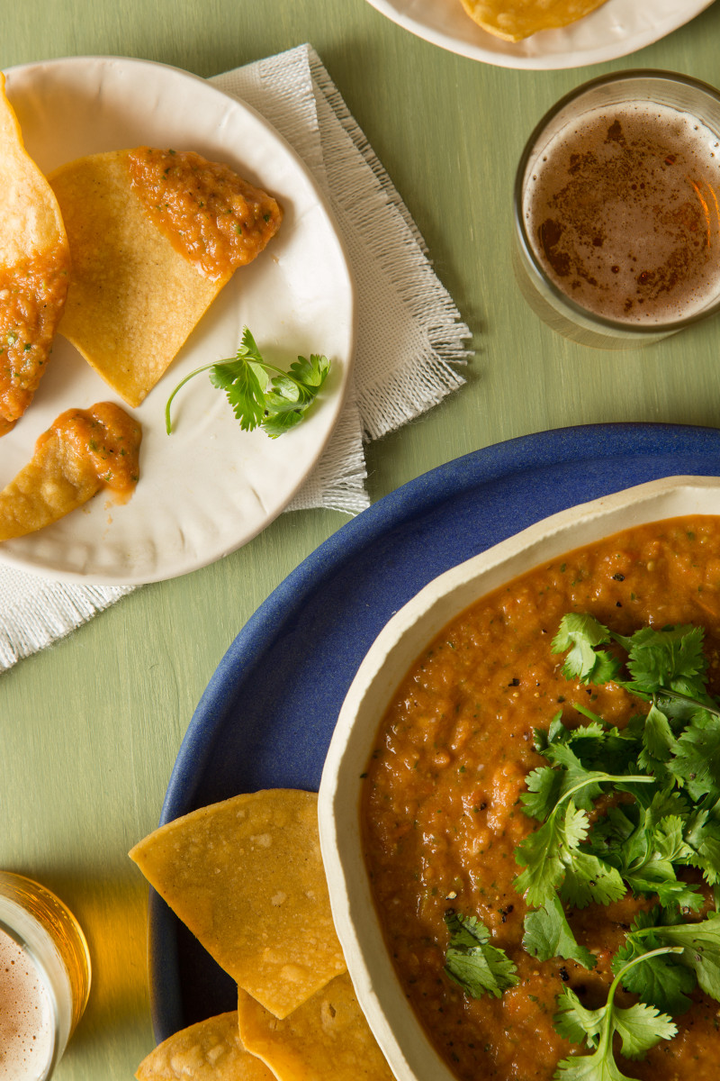 Tomato salsa in a bowl with a plate of tortilla chips with salsa on them.