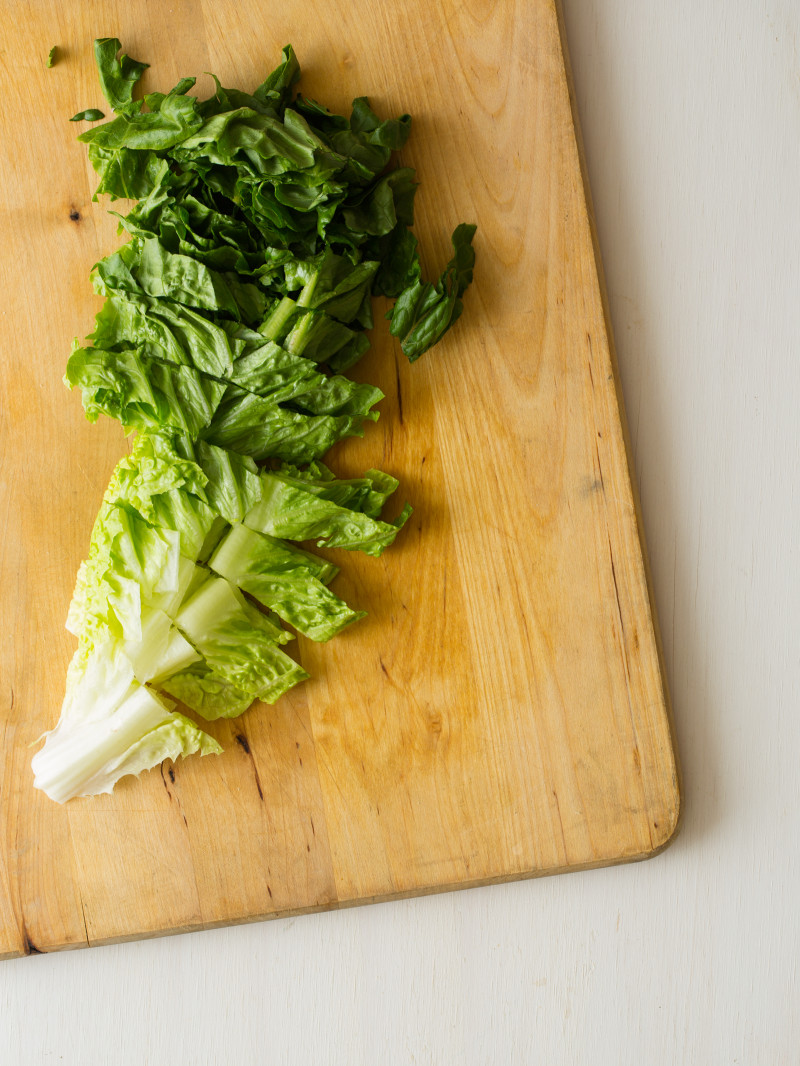 A whole large romaine heart sliced from top to bottom on a wooden cutting board.
