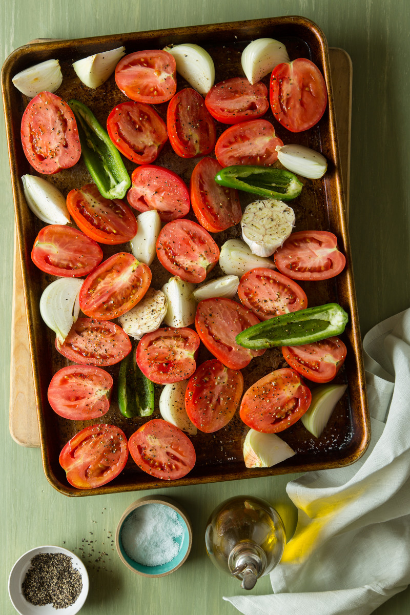 Ingredients for roasted tomato salsa on a baking sheet with salt and pepper on top.
