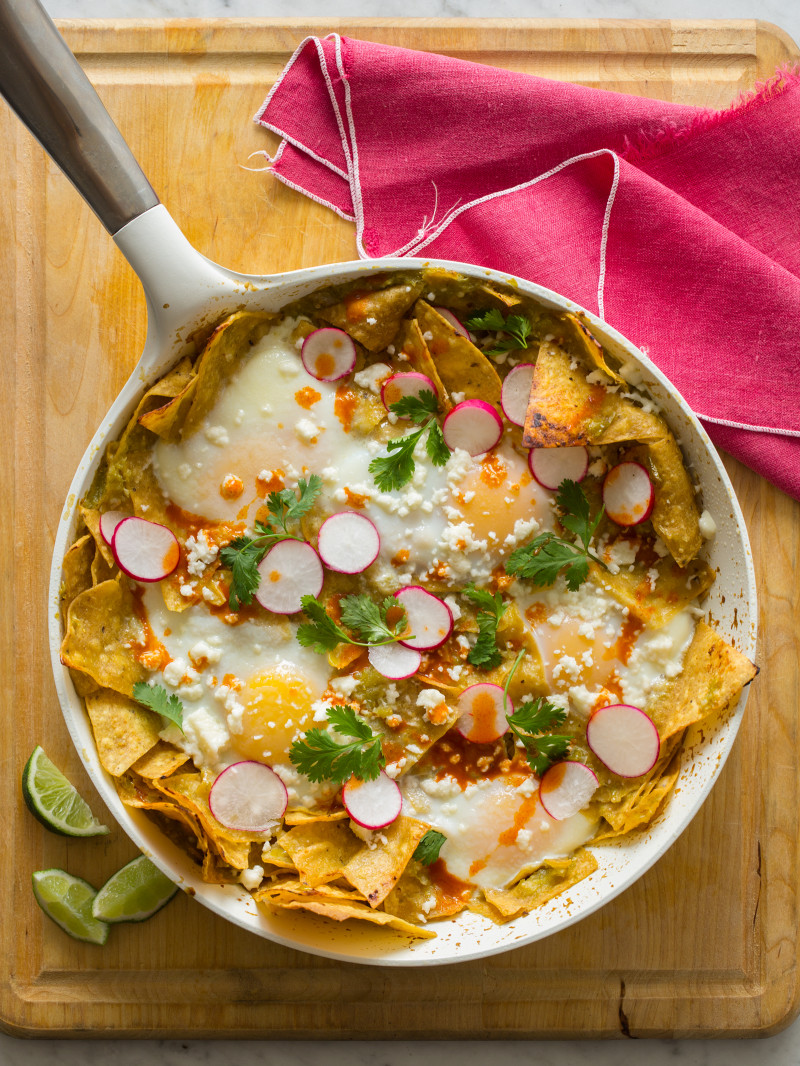 Green chilaquiles in a pan on a wooden surface with a pink linen.