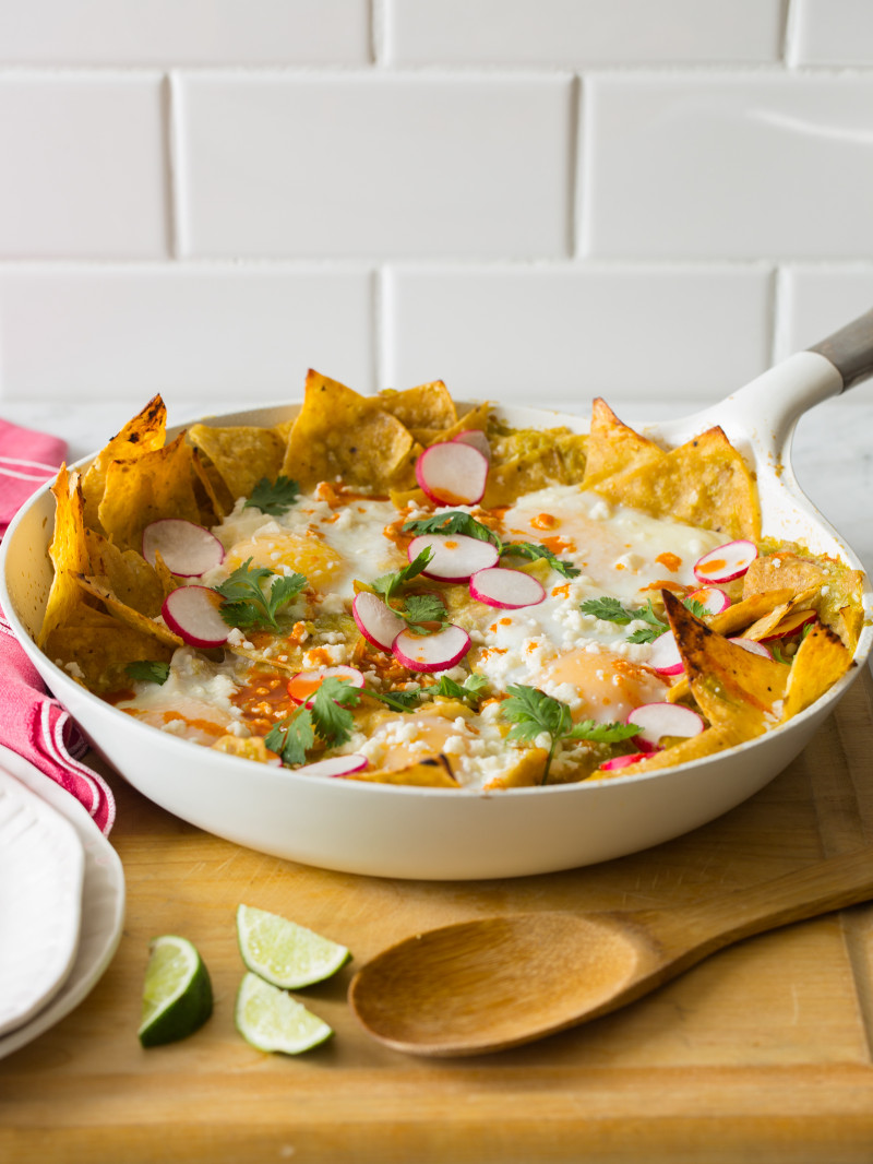 Green chilaquiles in a pan on a wooden surface with a wooden spoon.