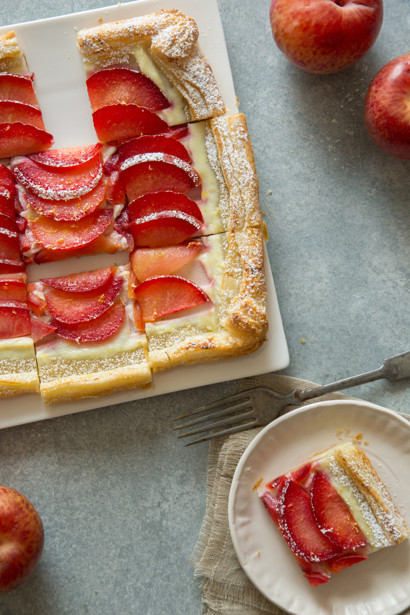 A sliced stone fruit tart with a slice on a small plate with a fork.