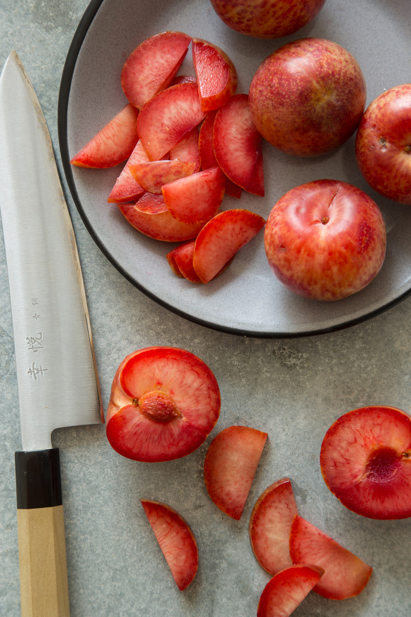 A plate of plums, both whole and sliced, with a knife.