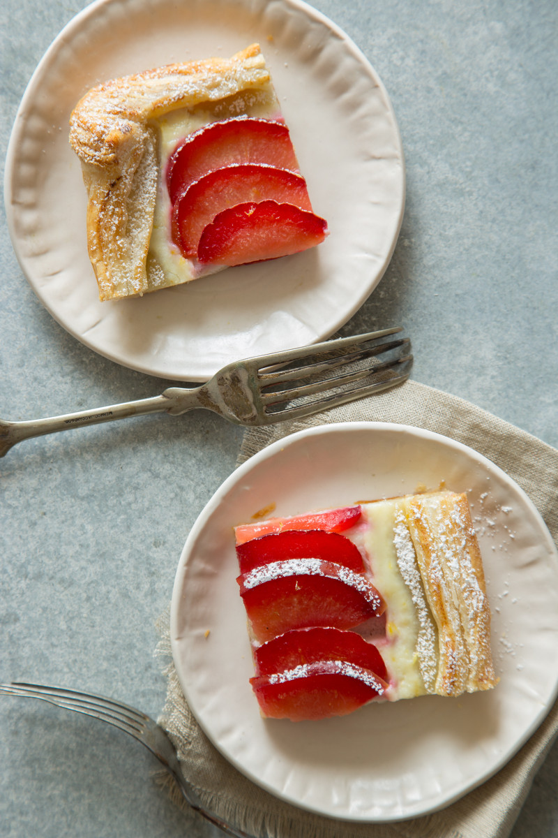 Slices of stone fruit tart on plates with a fork and napkin.