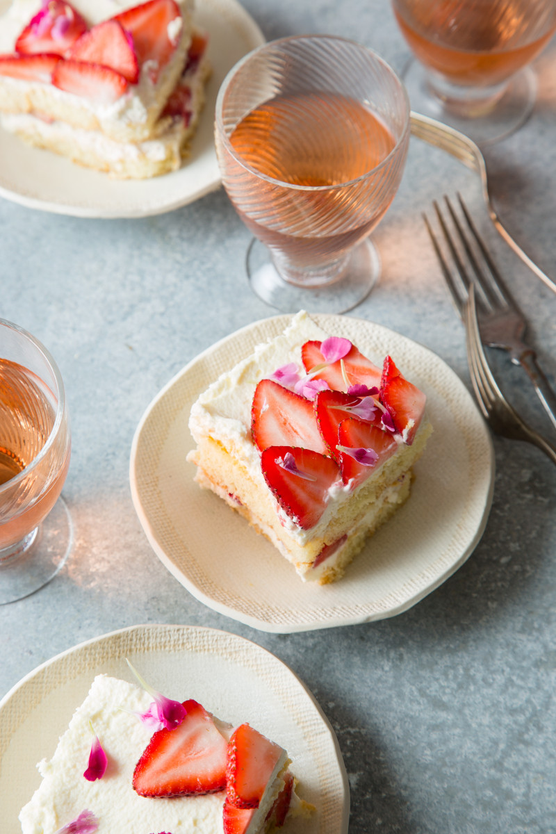 A piece of strawberry tiramisu on a small plate with forks and drinks.