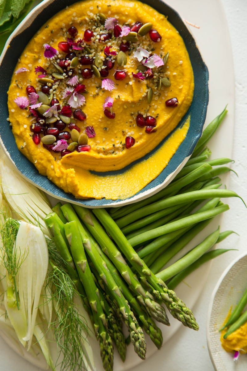 A close up of a bowl of roasted pumpkin hummus with a variety of veggies.