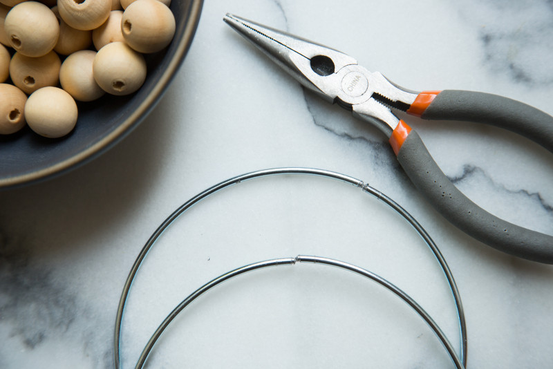 A close up of a bowl of wooden beads, wire cutters, and cut wire rings.