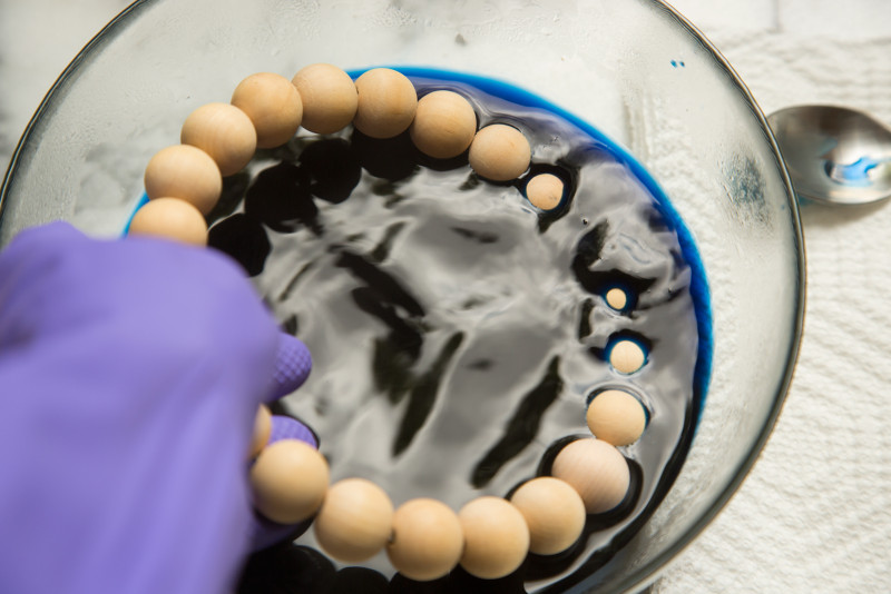 Beaded wire rings being dipped in a bowl of dye by a gloved hand.