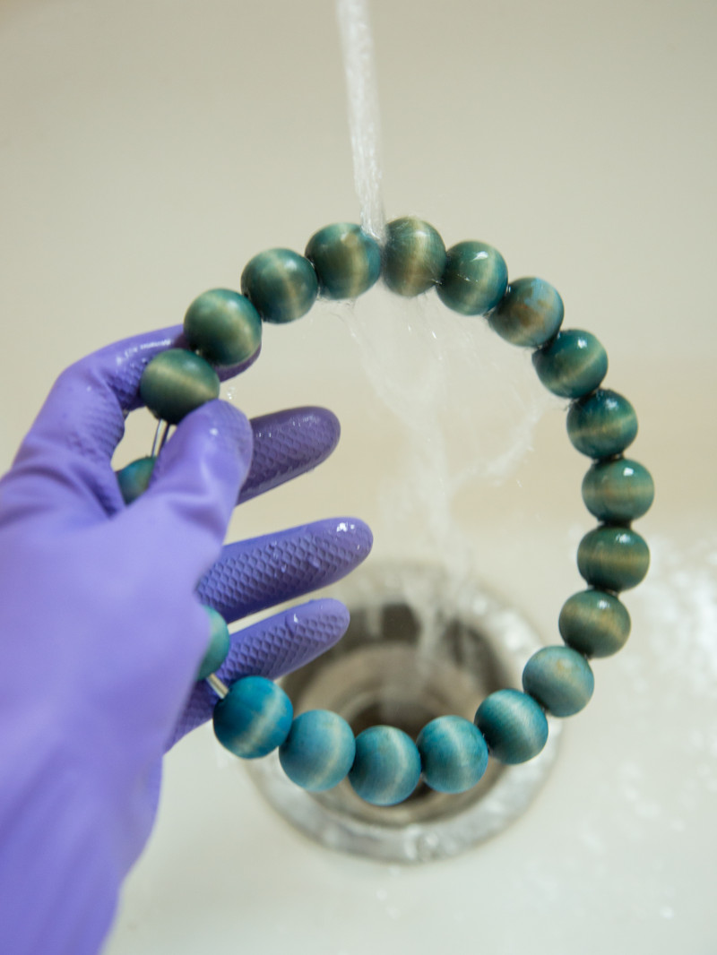 Dyed beaded towel rings being rinsed off under a tap with a gloved hand.