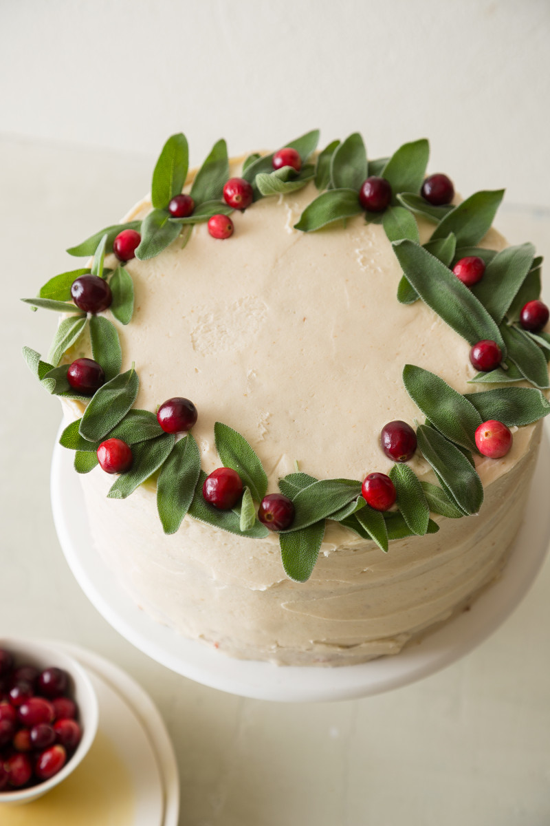 The top of an apple cranberry cake decorated with fresh cranberries and sage.