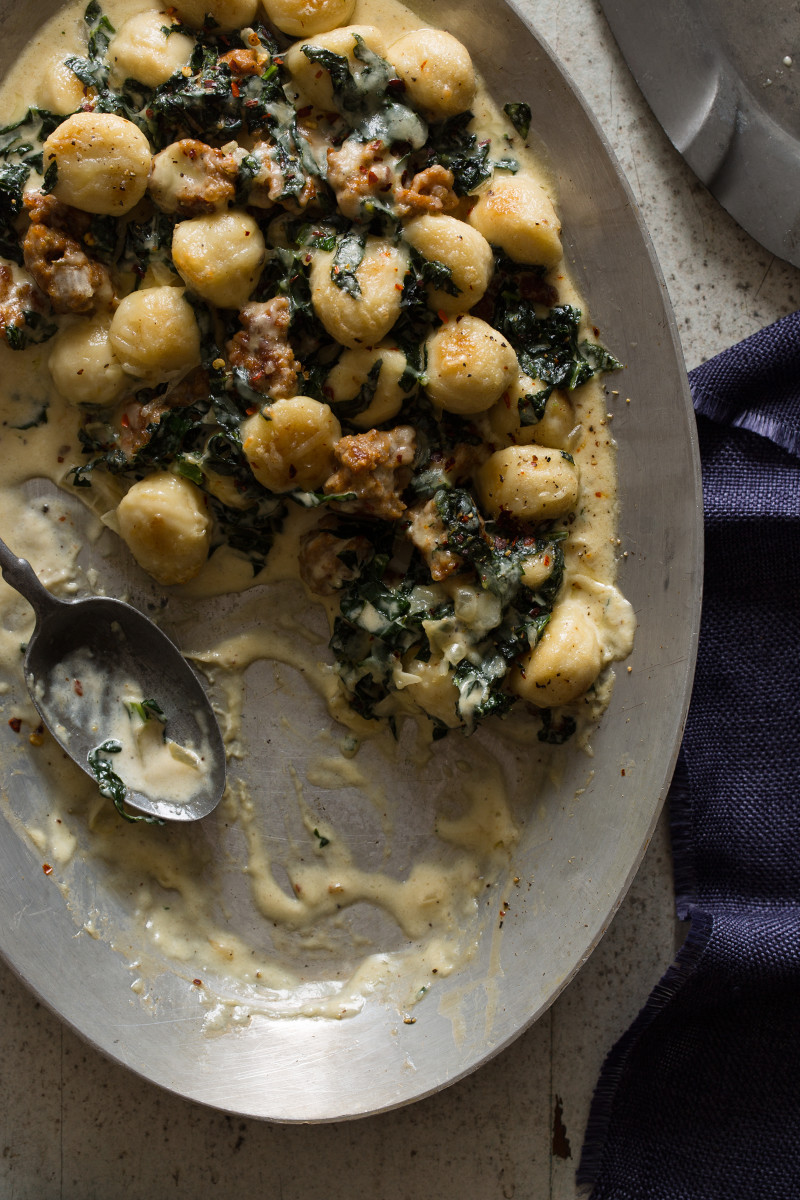 A close up of sausage and kale baked gnocchi with a portion gone and a spoon.