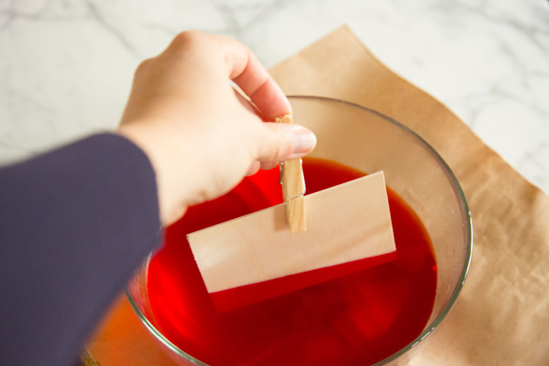 a hand dipping the place card into dye using a clothes pin