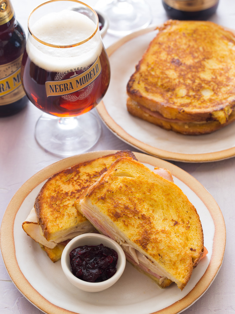 Plates of Monte Cristo sandwich with cranberry jam next to a beer.