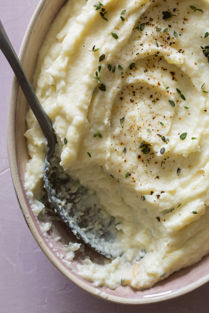 A close up of cauliflower, parsnip, and roasted garlic mash in a bowl with a spoon.