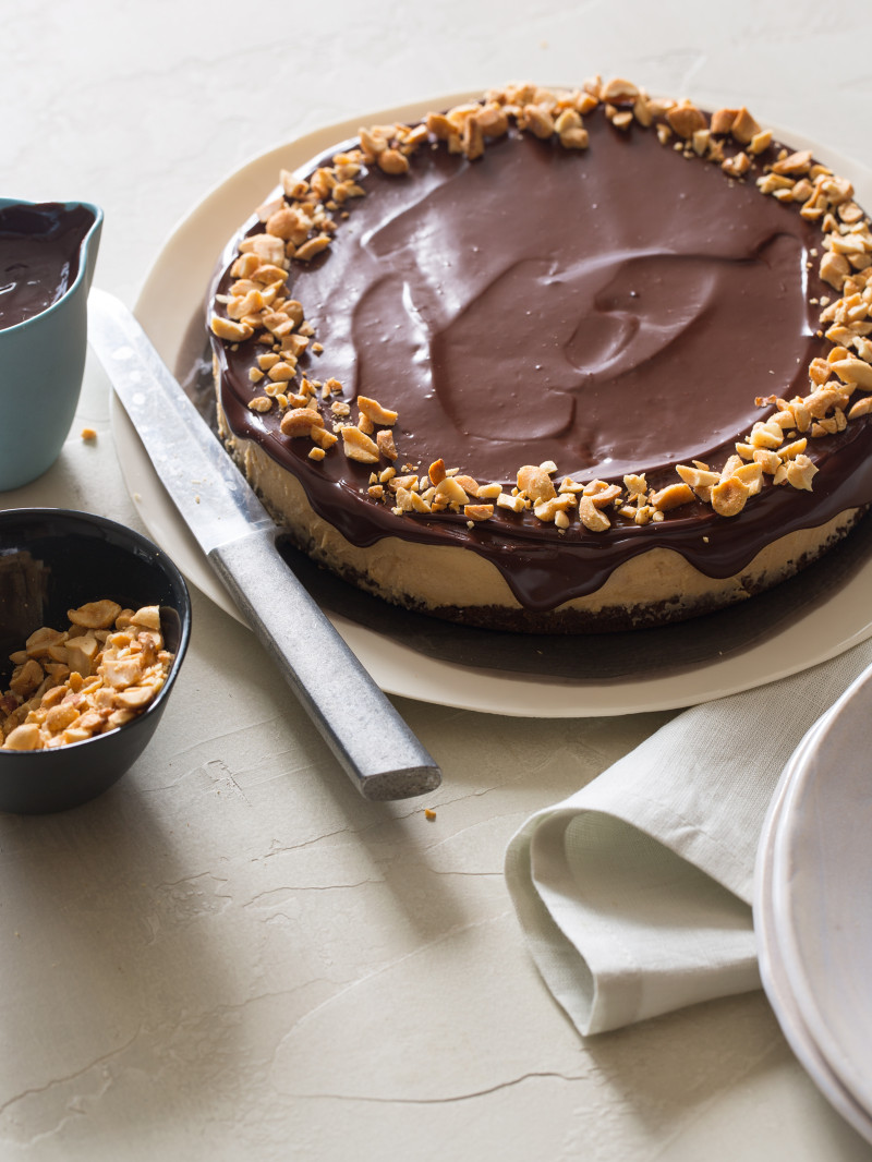 A no bake peanut butter cheesecake with dark chocolate ganache with plates and a knife.