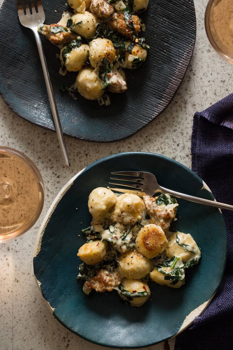 Plates of sausage and kale baked gnocchi with forks and a drink.