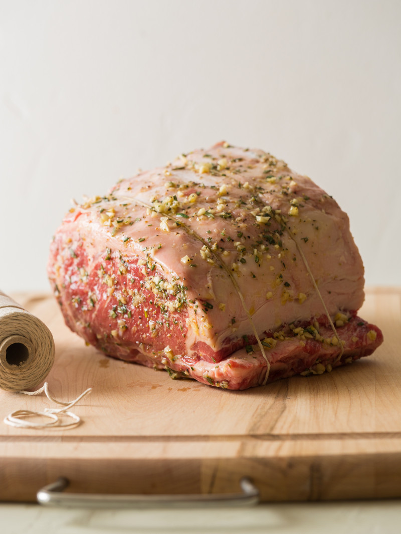 A raw rib roast seasoned and tied with twine on a wooden cutting board.