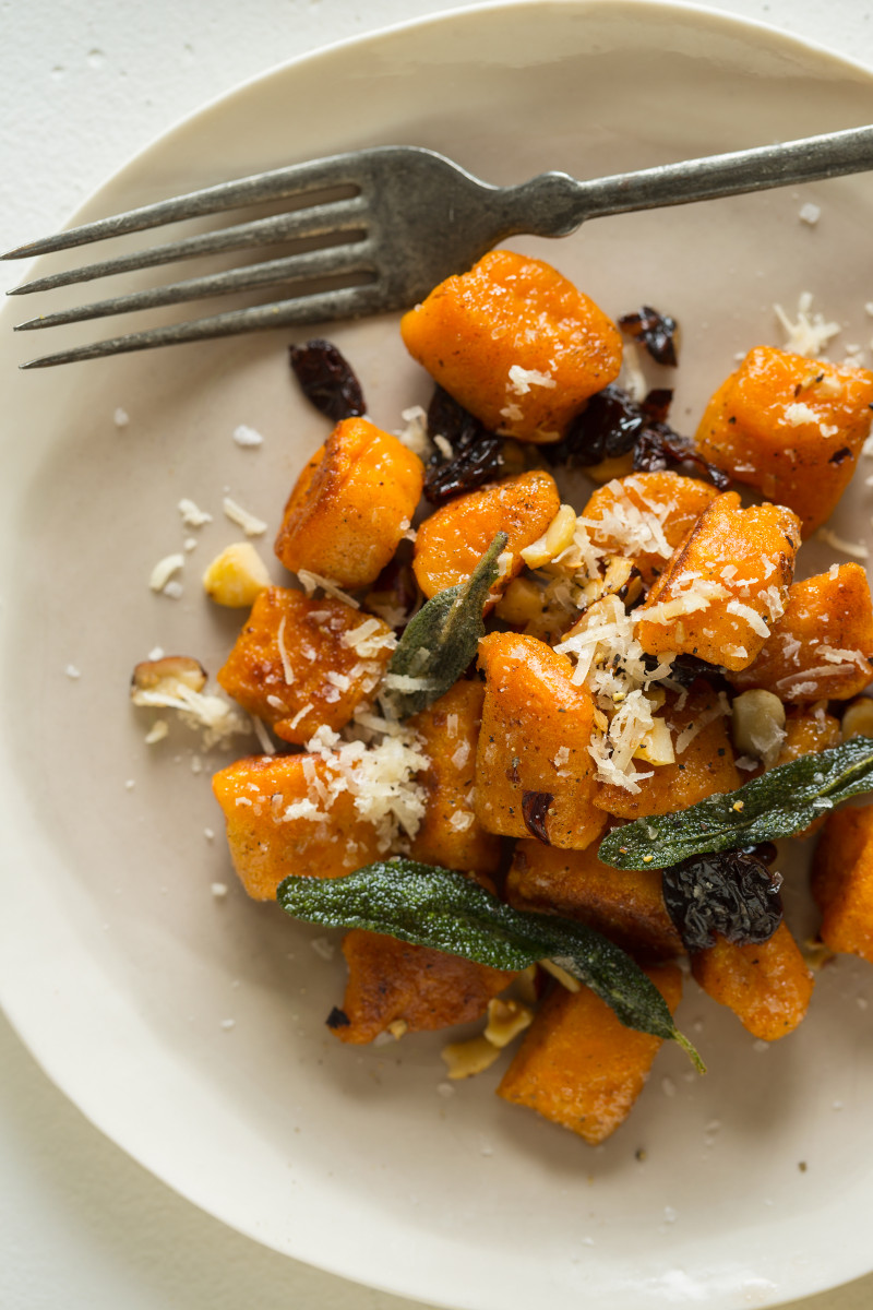 A close up of sweet potato gnocchi with fried sage dried cherries and toasted hazelnuts.