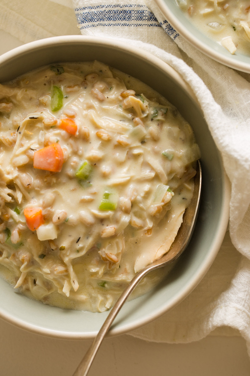 A close up of creamy chicken and faro soup in a bowl with a spoon.