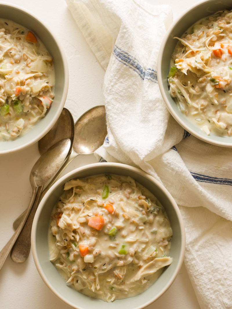 Creamy chicken and faro soup in bowls with linens and spoons.